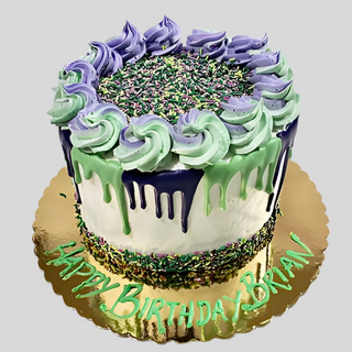 A custom round Sprinkle Rainbow cake with white frosting, green and purple drip icing, piped swirls, and colorful sprinkles on the center and base. "Happy Birthday Brian" is written in green on the gold cake board.