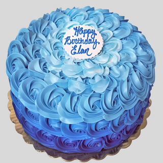 A round Ombre Tones birthday cake with blue rosette icing and a white plaque reading "Happy Birthday Elan" in blue lettering, perfect for specialty occasions, displayed on a gold cake board.