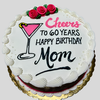 Cosmo Cheers is a round white birthday cake topped with a pink cocktail glass, three pink roses, and “Cheers to 60 years, Happy Birthday Mom” in pink and black icing—a beautiful cake for a memorable celebration.