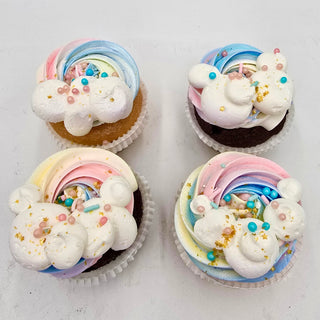 Rainbow Clouds: Four cupcakes with pastel rainbow swirled frosting, white cloud-like dollops, colorful sprinkles, and edible gold stars, arranged on a white surface.