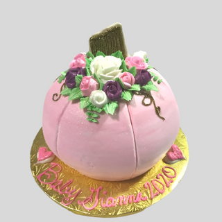 The Pink Pumpkin is a pumpkin-shaped cake in pink, topped with colorful frosting flowers and a gold stem. It sits on a gold board with “Baby Gianna 2020” written in pink icing at the base.