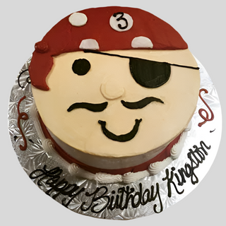 Celebrate your child's birthday with the Pirate Face cake! This custom cake features a pirate with a red bandana, black eyepatch, mustache, and the number 3. "Happy Birthday Kingston" is written on the silver cake board.