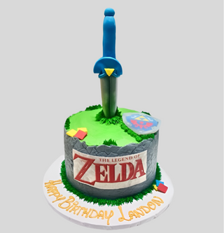A round cake decorated with the Zelda Sword theme, featuring a sword and shield topper, stone-like pattern, and "Happy Birthday Landon" on the base—perfect for kids who love adventure!.