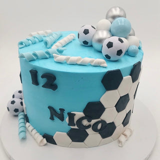 The "Soccer Party" cake is blue, features hexagon soccer ball designs, white and blue candy spirals, silver and black sphere candies, and has "12" and "NICO" written on the side.