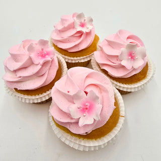 Four Cherry Blossom Cupcakes topped with pink swirled frosting and adorned with delicate white and pink flower-shaped sugar decorations, arranged on a white surface.