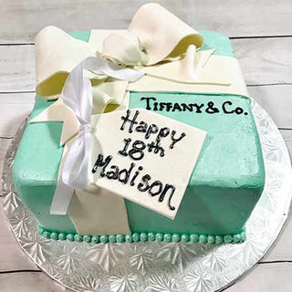 Inspired by the Tiffany Box, this square birthday cake features blue icing, a white ribbon, and a "Happy 18th Madison" gift tag, all presented on a silver board.