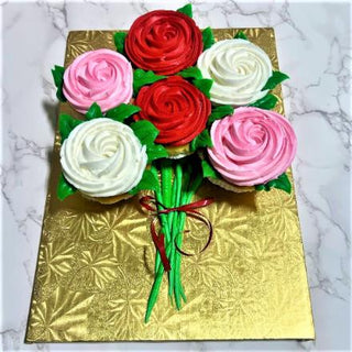 Love Bouquet: Red, pink, and white frosted cupcakes arranged as flowers on a gold textured board with green icing stems, leaves, and a red ribbon.