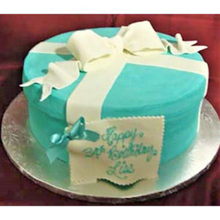 The Tiffany Round specialty birthday cake features a turquoise gift box design with a white ribbon, bow, and tag reading "Happy 34th Birthday, Lisa" in blue icing. This custom cake is presented on a silver board.