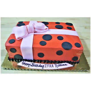 A custom Sheet Present cake, rectangular and red with black polka dots, a large pink fondant bow, and a white tag reading “Happy Birthday IFRA Kuttima,” resembles a gift box.