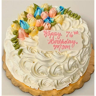 The Flower Rosette cake features white flower rosettes, colorful frosting flowers, and a white plaque with “Happy 76th Birthday Mom” in pink—a beautiful specialty birthday design.