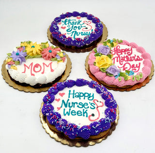 Four round Cookie Cakes with colorful icing, customizable decorations, and messages: “Thank You Nurses!”, “Mom”, “Happy Mother’s Day”, or “Happy Nurse’s Week,” topped with flowers, sprinkles, and chocolate chip accents.