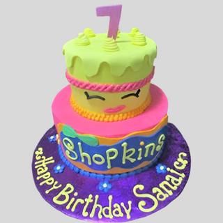 The Shopkins Tier is a two-tiered, colorful kids cake featuring a cute face, number 7 topper, and "Happy Birthday Sanaia" on a purple base—perfect for any themed birthday party.