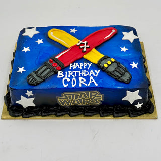 The Star Wars Lightsabers cake is a rectangular birthday treat featuring two crossed lightsabers, white stars, and "Happy Birthday Cora" on a blue background with the Star Wars logo on the front.