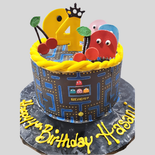 The Pac Man cake features colorful ghosts, cherries, a yellow 24 topper, and "Happy Birthday Hasani" in yellow icing on a black board—perfect for celebrating kids' birthdays with this custom Pac Man design.