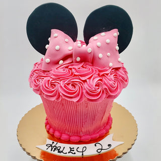 The Minnie Smash custom cake is shaped like a cupcake, decorated with frosting roses, black fondant ears, a pink polka dot bow, and features Haley’s name with the number 2 on a white plaque—perfect for kids!.