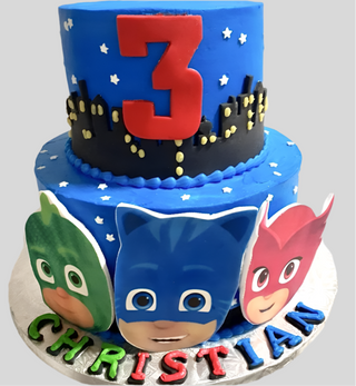 The PJ Masks Tier is a two-tier cake featuring a red number 3, cityscape, and PJ Masks character faces. CHRISTIAN is spelled in colorful letters at the base—ideal as a custom kids birthday cake for PJ Masks fans.