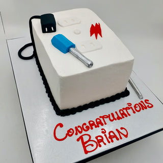 The Electrician Outlet cake is designed as a white outlet with a black cord, blue screwdriver, and red lightning bolt, displayed on a board that says "Congratulations Brian" in red icing.