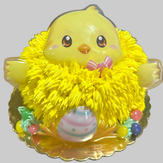 The "Baby Chick" cake features a cute yellow chick with big eyes, fluffy fur, a pink bow, and an Easter egg in front, surrounded by colorful candies on a gold tray.