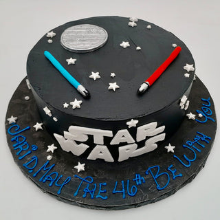 The Star Wars Birthday cake is round and black with white stars, a gray Death Star, a red and blue lightsaber, STAR WARS on the side, and "JARID, MAY THE 46TH BE WITH YOU" in blue icing at the base.