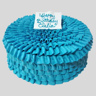 The Ruffled Solid is a custom cake featuring bright blue ruffled icing and a white plaque on top with “Happy Birthday Clelia” written in blue.