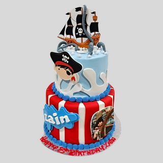 Pirate Boy is a two-tier custom cake with a ship topper, waves, and a pirate face. The red and white striped bottom tier displays Zain’s name with a pirate image, and “Happy 5th Birthday Zain” is written in red icing on the base.
