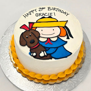 Madeline Dog cake with white frosting, yellow trim, and an image of a girl in a yellow hat and blue outfit hugging a brown dog. Top text: "Happy 3rd Birthday Gracie!.
