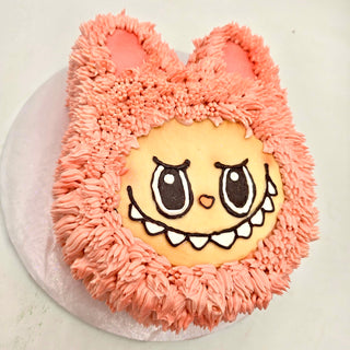Labubu Smile is a round cake designed as a cute, cartoonish pink animal face with big eyes, pointy ears, and a wide grin, all covered in fluffy pink icing to mimic fur.