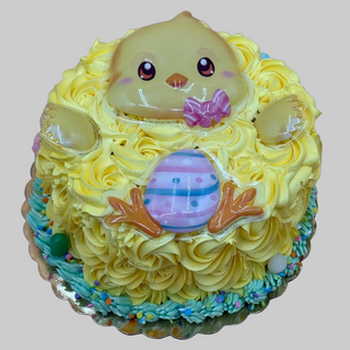 The Easter Chick cake is round with yellow frosting, a chick face, pink cheeks, a pink bow tie, and an egg with pastel stripes. Colorful sprinkles decorate the base.