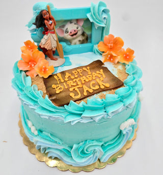 The Moana Motif features a blue frosted birthday cake topped with orange flowers, a "Happy Birthday Jack" plaque, and Moana and Pua figurines from Disney’s Moana as decorations.