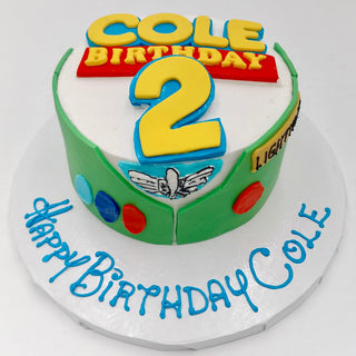 Toy Story Fondant round birthday cake with a Buzz Lightyear theme, number 2 topper, Cole Birthday message, colorful buttons, and "Happy Birthday Cole" in blue icing on the board.
