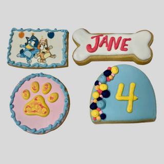 Paw Patrol Cookies: Four decorated cookies featuring cartoon dogs, a bone with "Jane," a round one with a paw print, and a hat-shaped cookie with the number 4 and colorful dots on light gray.