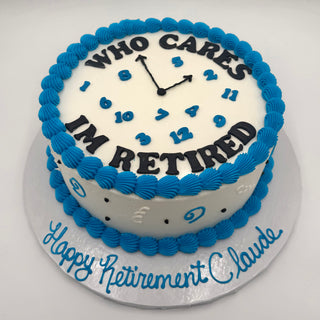 The “Retired Clock” is a round white cake with blue frosting edges and a clock face set at 3:00. It says “WHO CARES I'M RETIRED” on top and “Happy Retirement Claude” in blue icing at the base.