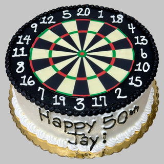A round Dart Numbers cake decorated like a dartboard with black, white, red, and green sections, featuring "Happy 50th Jay!" in gold icing on the side.