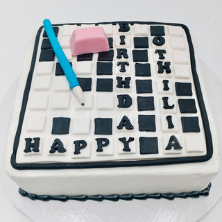 A cake designed like a Scrabble Game board, featuring the words HAPPY BIRTHDAY OTHILIA—ideal for any Sports & Hobby enthusiast—and topped with a blue fondant pen and pink fondant eraser.