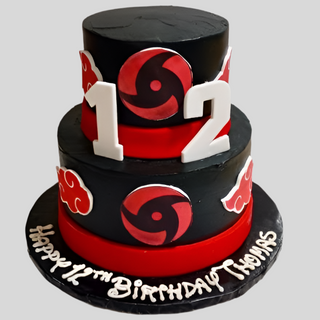 A custom kids' cake: a two-tiered black and red birthday cake topped with large white 12s, decorated with Ninja Logo, and "Happy 12th Birthday Thomas" written in white icing at the base.
