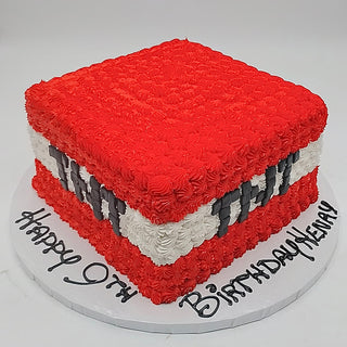 A square Minecraft Box cake with red, white, and black icing to resemble a TNT block sits on a round board with "Happy 9th Birthday Kevin" written in black icing.