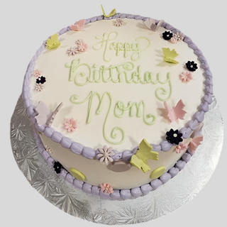The Butterfly Simple is a round specialty birthday cake featuring "Happy Birthday Mom" in green icing, purple frosting borders, pastel flowers, and butterfly-shaped decorations, all presented on a silver cake board.