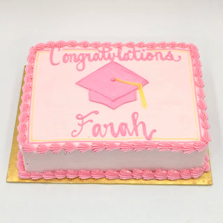 A rectangular pink "Grad Cap" cake with piped borders, a pink graduation cap with yellow tassel, and "Congratulations Farah" written in pink icing.