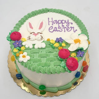 The Easter Basket is a round cake decorated with a piped bunny, colorful flowers, "Happy Easter" in purple icing, basket-weave green frosting, and jelly beans around the base.