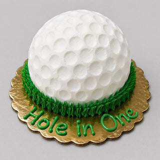 Golf Smash is a round custom cake designed like a white golf ball with dimples, set on green icing grass. "Hole in One" is written in green icing on a gold board—ideal for birthdays or baby showers.