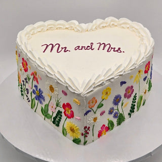 Bridal Heart: Heart-shaped cake with white frosting, "Mr. and Mrs." in pink on top, colorful hand-painted flowers on the sides, and a scalloped frosting border.