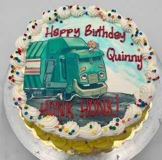 Round birthday cake with white frosting, colorful sprinkles, and yellow trim featuring the Trash Truck Scan image of a smiling child driving a green garbage truck, with "Happy Birthday Quinny HONK HONK!" in red text.