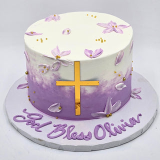 The Religious Beauty is a round cake with white and purple ombre frosting, gold beads, purple flowers, and a gold cross. "God Bless Olivia" is written in purple icing on the cake board.