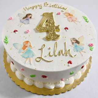 Fairy Girls birthday cake: round, white frosting, topped with four fairies, red and pink flowers, green leaves, a large gold “4”, and "Lilah" in gold. "Happy Birthday" is written on top.