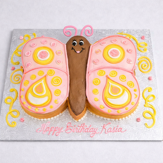 Butterfly Smile: A custom cake shaped like a colorful butterfly with pink, yellow, and orange icing, a cheerful smile, and "Happy Birthday Kasia" written in pink. Perfect for fans of animal-themed cakes!.