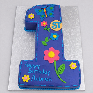 The Butterfly Number cake, shaped like a 1 and topped with colorful flowers, a butterfly, and "Happy Birthday Aubree" on a silver board, is the perfect personalized cake for any celebration.