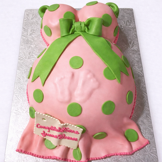 The Pink Belly cake is shaped like a pregnant belly with pink and green polka dots, topped with a large green bow. A small plaque reads, "Congratulations Janna, Jenna & Simara.
