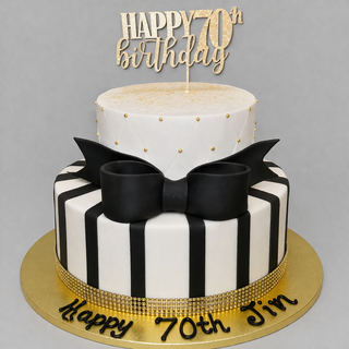 A custom two-tier "Bow Black" cake: top tier white with gold dots, bottom tier black and white stripes, decorated with a male bow. “Happy 70th Jim” is on the gold board and finished with a celebratory topper.