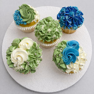 Five Hydrangea Mixed cupcakes feature intricate green, white, and blue floral frosting with silver pearl sprinkles. Arranged in a circle on a white textured surface, they're perfect for specialty birthday designs.
