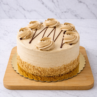The Salted Caramel Layer Cake features light brown dulce de leche buttercream frosting with top rosettes, diagonal chocolate drizzle, and a crumb-coated lower edge. Presented on a wooden board with a scalloped gold base.